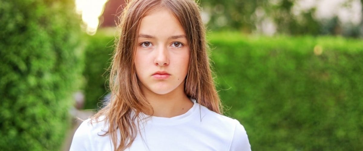 nominated-close-up-portrait-of-serious-angry-teenager-girl-outdoors-in-park-with-green-hedge_t20_JzeyN4